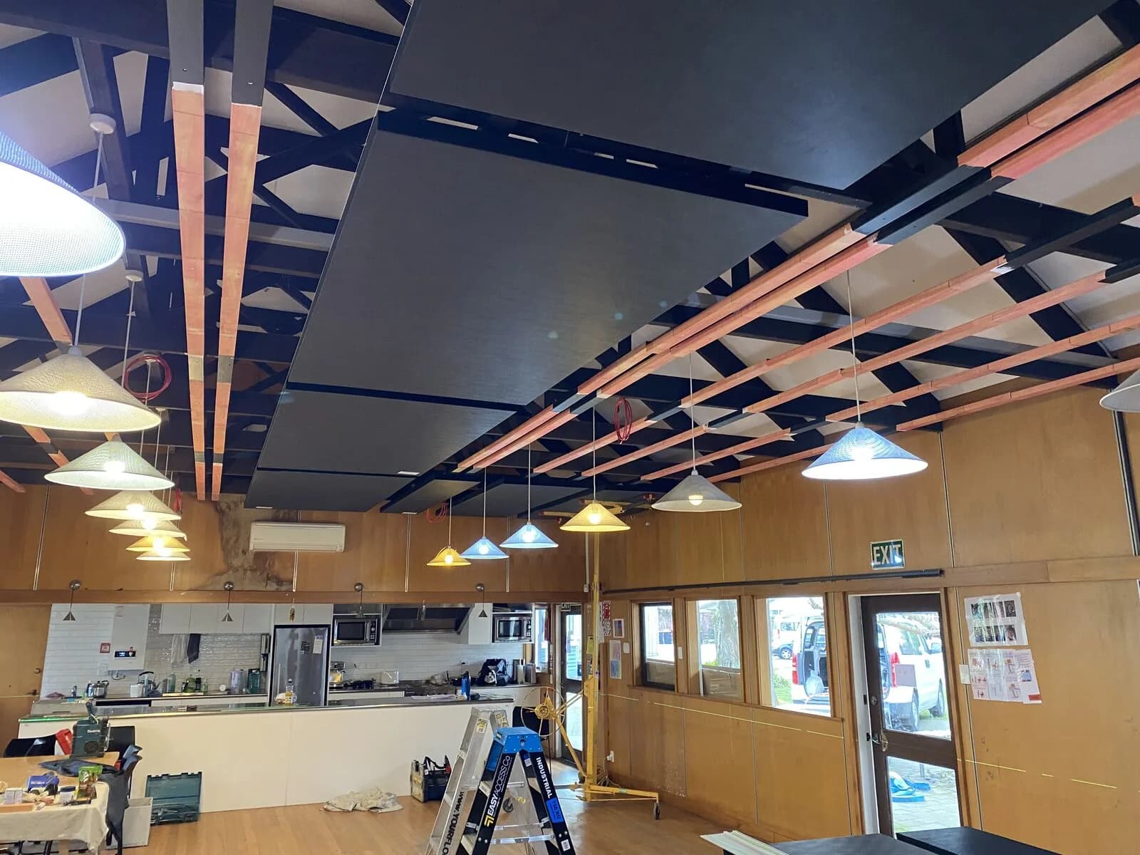 Exposed black truss ceiling with acoustic panels going in above the Hopepa kitchen