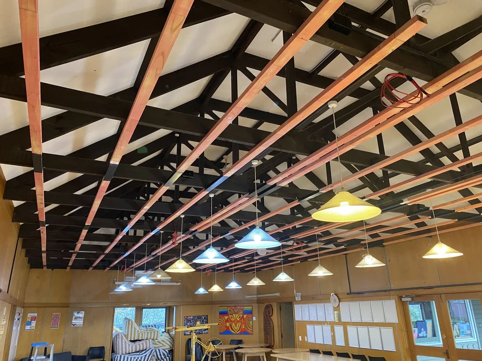 Exposed black steel truss and timber-batten ceiling with white pendant lights over the Hopepa dining hall