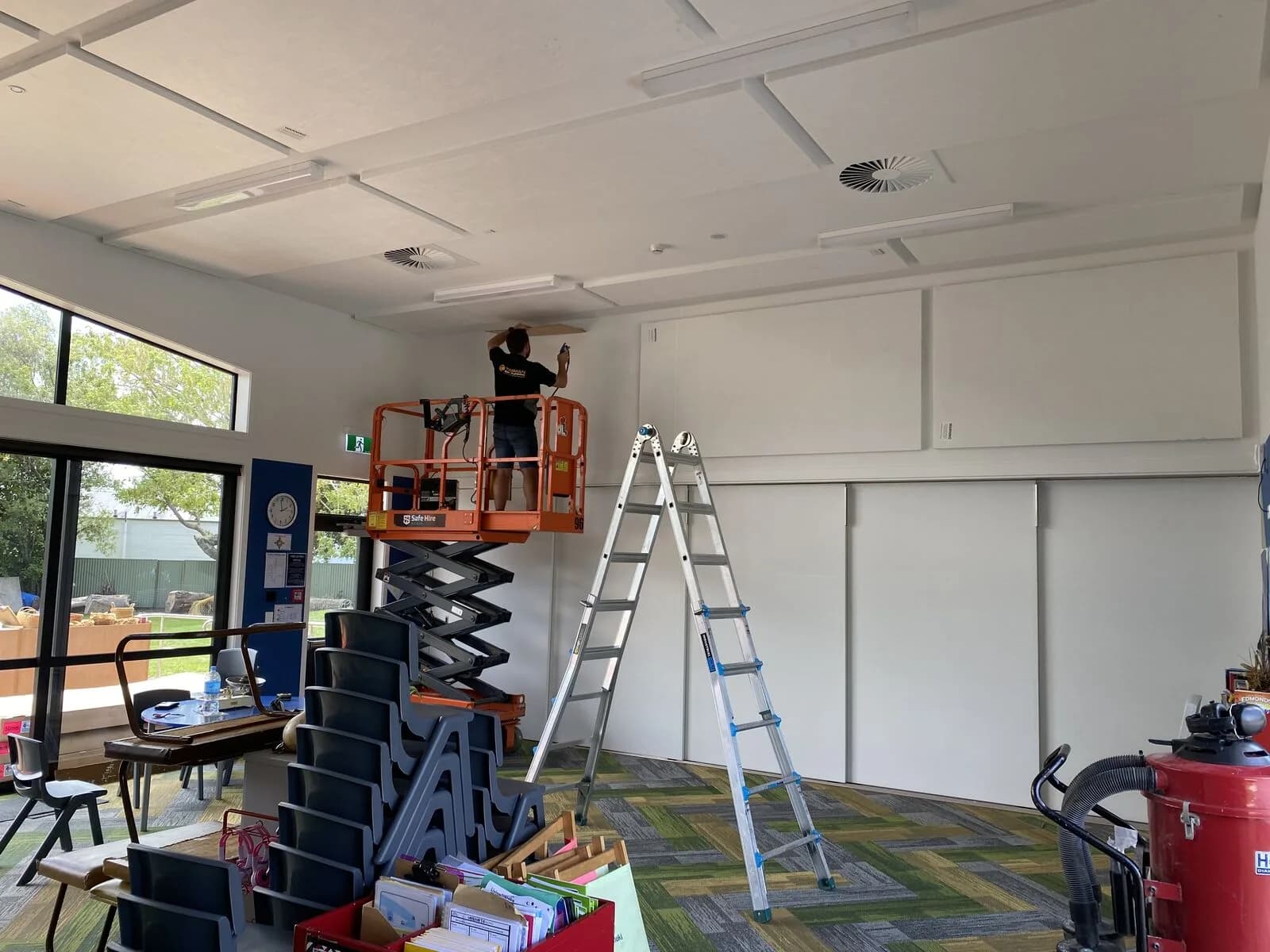 Acoustic ceiling install from an orange scissor lift and step ladder at Parklands School