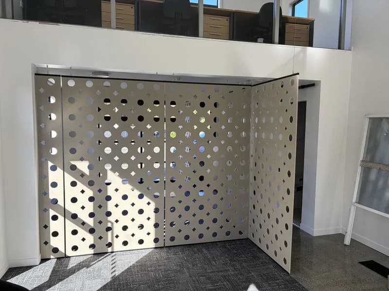 White perforated suspended acoustic screens dividing the Ray White office, sunlight casting dot shadows on grey carpet