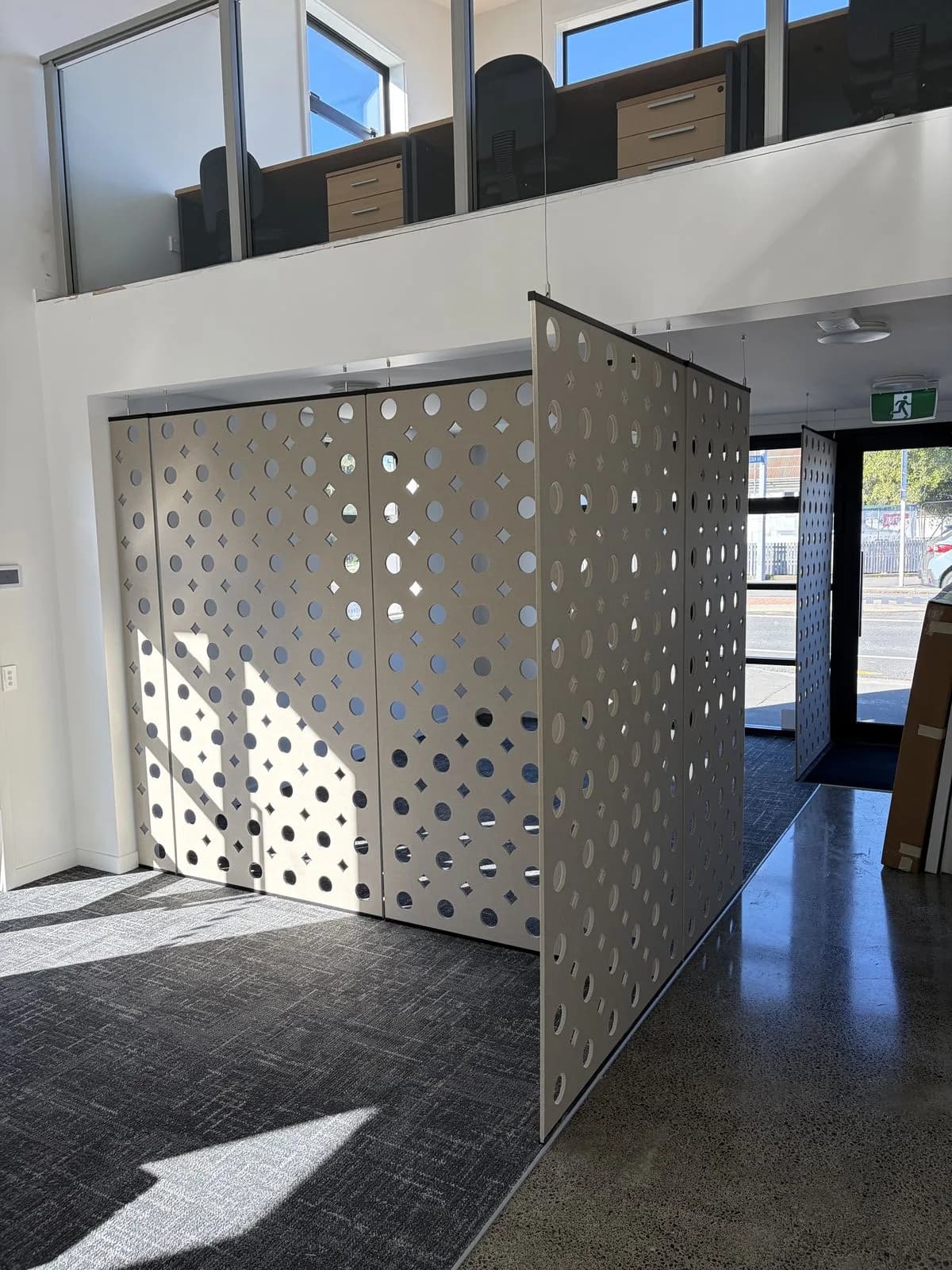 Perforated suspended acoustic partitions in the Ray White open-plan office over grey carpet