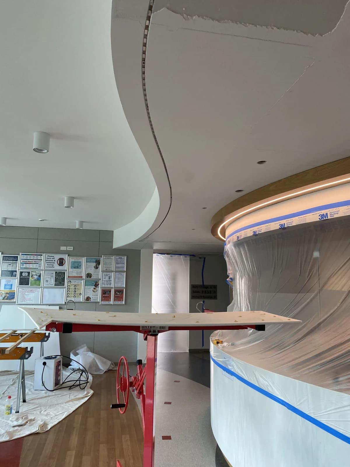 Double-curve ceiling under construction with red steel props and plastic sheeting at Riccarton Doctors