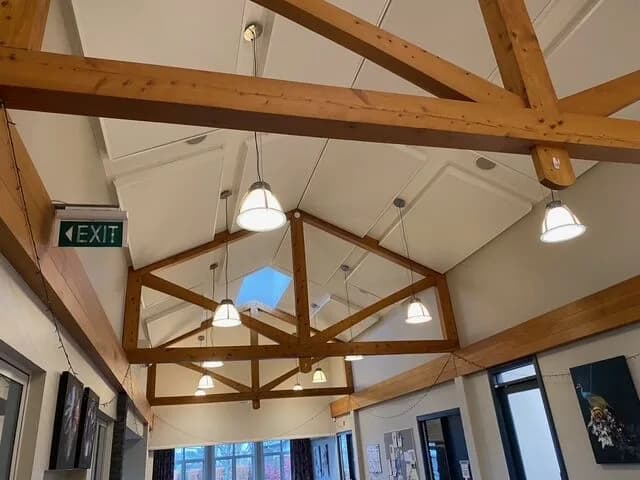 Vaulted timber-truss ceiling with white acoustic panels and pendant lights, Somerset activity building