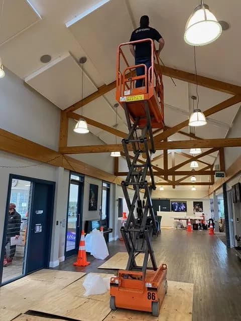 Acoustic ceiling install in progress from an orange scissor lift under the Somerset vaulted timber trusses